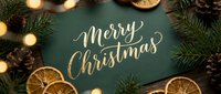 Merry Christmas gold calligraphy on green card surrounded by pine cones, dried orange slices, fir branches, and warm bokeh lights.