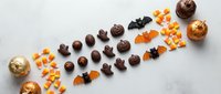 Halloween chocolate candies and orange sweets arranged in decorative line on white marble background for seasonal confectionery and holiday treats.