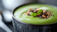 Fresh green smoothie bowl topped with nuts seeds and mint leaves served in dark ceramic bowl for healthy breakfast nutrition.