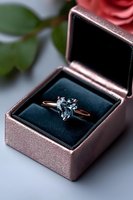 Heart-shaped aquamarine engagement ring in rose gold setting displayed in velvet ring box with pink rose petals in background, romantic proposal setup.