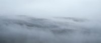 Misty mountain landscape with rolling hills covered in dense fog and clouds creating atmospheric layers of gray and white tones for nature backgrounds.