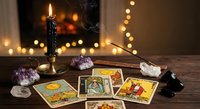 Mystical tarot cards spread on wooden table with burning candle, crystals and warm bokeh lights creating atmospheric fortune telling scene for spiritual guidance.