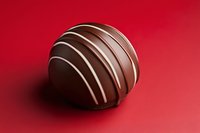 Luxury dark chocolate truffle with white stripe decoration on vibrant red background, close-up shot for confectionery and Valentine's Day designs.