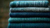 Stack of cozy knitted sweaters in blue and teal tones with various cable and textured patterns for autumn winter fashion and seasonal clothing concepts.