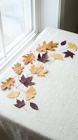 Autumn leaves scattered on white linen fabric near window creating cozy seasonal home decor arrangement for fall interior design and crafting projects.