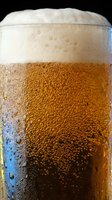 Chilled cola beverage in glass with condensation droplets, golden carbonated liquid, and thick foam head against dark background for beverage advertising and refreshment concepts.