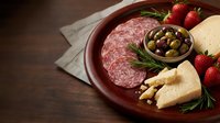 Gourmet charcuterie board with sliced salami, aged cheese, fresh strawberries, olives and rosemary on rustic wooden plate for entertaining and appetizers.