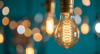 Vintage Edison bulb glowing with warm filament against teal background with golden bokeh lights creating cozy atmospheric lighting for interior design.