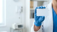 Healthcare professional in white coat and blue latex gloves holding blank white card in modern medical clinic or laboratory setting for business messaging.