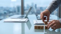 Professional businessman hands arranging wooden blocks with gear icons on modern office desk overlooking city skyline for business strategy concepts.