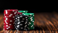Stacks of poker chips in red, black and green colors on rustic wooden table with dramatic lighting and shallow depth of field, casino gaming concept.