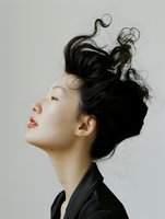 Young Asian woman with messy updo hairstyle and red lips in profile view against light background, wearing black jacket. Artistic portrait showing serenity and style.
