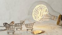 Glowing brain filament inside light bulb with miniature shopping carts representing creative commerce and innovative retail marketing solutions.