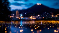 Dreamy night cityscape with glowing bokeh lights reflecting on wet surface, creating magical atmosphere against dark blue sky and illuminated urban silhouette.