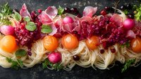 Fresh rice noodles garnished with citrus, radishes, pomegranate seeds and herbs on dark background. Vibrant Asian fusion cuisine composition for food service.