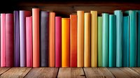 Colorful book spines arranged in rainbow spectrum order standing on wooden shelf against dark background, creating vibrant gradient display for education and reading.
