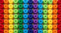 Colorful rainbow yarn balls arranged in neat rows creating vibrant gradient pattern for crafting and textile projects on white background.