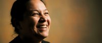Happy Asian woman smiling warmly with genuine joy and positive expression against soft blurred background for lifestyle and wellness content.