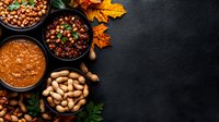 Autumn food composition with peanuts, chickpeas, beans and lentil curry in bowls on dark background with maple leaves and copy space for menu design.