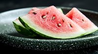 Fresh watermelon slices with bright pink flesh and black seeds on dark plate with water drops, dramatic lighting creates appetizing food photography.