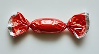 Red wrapped candy in shiny metallic foil wrapper with twisted ends on white background, isolated sweet treat for confectionery and holiday designs.