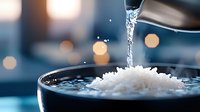 Clear water stream pouring onto white rice grains in glass bowl with bokeh lights background creating splash effect, macro food photography.