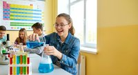 Young female student conducting chemistry experiment with colorful liquids in school laboratory classroom setting for educational science learning.