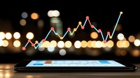 Holographic financial chart projection from smartphone screen showing market growth trend analysis with blurred city lights background at night.