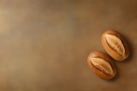 Freshly baked oval bread rolls with crispy crust on warm brown background, perfect for food menu or bakery advertising.