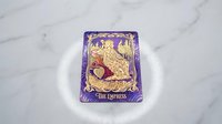 Ornate tarot card The Empress with golden decorative artwork on purple background placed on white marble surface for divination and spiritual guidance.