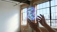 Professional hands interacting with holographic geometric sphere in modern loft office space with industrial windows for technology and innovation concepts.