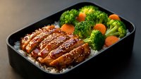 Glazed teriyaki chicken with steamed broccoli and carrots over rice in black bento box. Healthy Asian meal prep lunch with balanced nutrition and colorful vegetables.