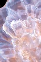 Macro view of translucent crystal formation with soft pink and blue hues against dark background, showing natural geometric patterns and light refraction effects.