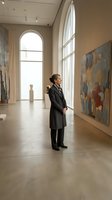 Woman in formal business attire viewing contemporary artwork in modern gallery space with natural light from tall arched windows, suitable for corporate, education, and cultural institution use.
