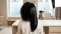 African American woman with natural curly and straightened hair halves showing hair transformation in modern bathroom mirror for beauty care.