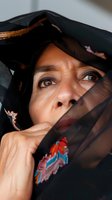 Middle-aged woman of South Asian descent wearing black sheer fabric with colorful embroidered details draped across her face, expressing contemplation and mystery for editorial and cultural storytelling projects.