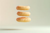 Three glazed donuts floating in air against light background, stacked vertically with soft shadows creating minimalist food composition for menu design.