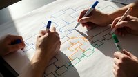 Business team collaborating on organizational chart planning with colorful markers on white paper during strategic meeting session.