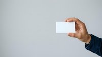 Male hand holding blank white business card against neutral gray background for corporate branding and marketing purposes.