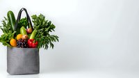 Fresh organic produce in gray textile shopping bag with vegetables, fruits and greens on white background, healthy food concept.