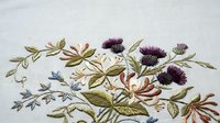 Delicate embroidered floral design featuring purple thistle flowers and green foliage on white fabric background for textile and craft projects.