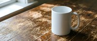 White ceramic coffee mug on rustic wooden table near window with natural lighting for morning beverage branding and kitchen product mockups.