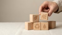 Businessman hand arranging wooden blocks with eco-friendly symbols including house, leaf, recycling and water drop representing sustainable business practices.