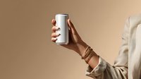 Hand holding blank white aluminum can against beige background. Female arm wearing beige blazer and wooden bracelets presenting beverage mockup.