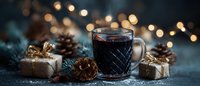 Festive mulled wine in glass mug surrounded by pine cones, wrapped gifts, and fir branches against blurred holiday lights background.