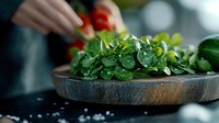Fresh watercress leaves in rustic wooden bowl with water drops and sea salt, selective focus on green herbs against dark background for food styling.