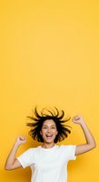 Joyful young woman with dark hair flying in motion, wearing white t-shirt, celebrating with raised fists against bright yellow background for lifestyle and happiness concepts.