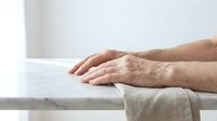 Elderly hands resting on white table surface showing aging skin texture and natural wrinkles in soft natural lighting for healthcare concepts.