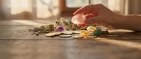 Woman hand selecting healing crystals and gemstones on wooden table with warm sunlight for spiritual wellness meditation and energy work practices.