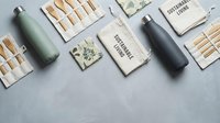 Flat lay composition featuring eco-friendly sustainable products including reusable water bottles, wooden matches, and notebooks on gray surface for branding and lifestyle marketing.